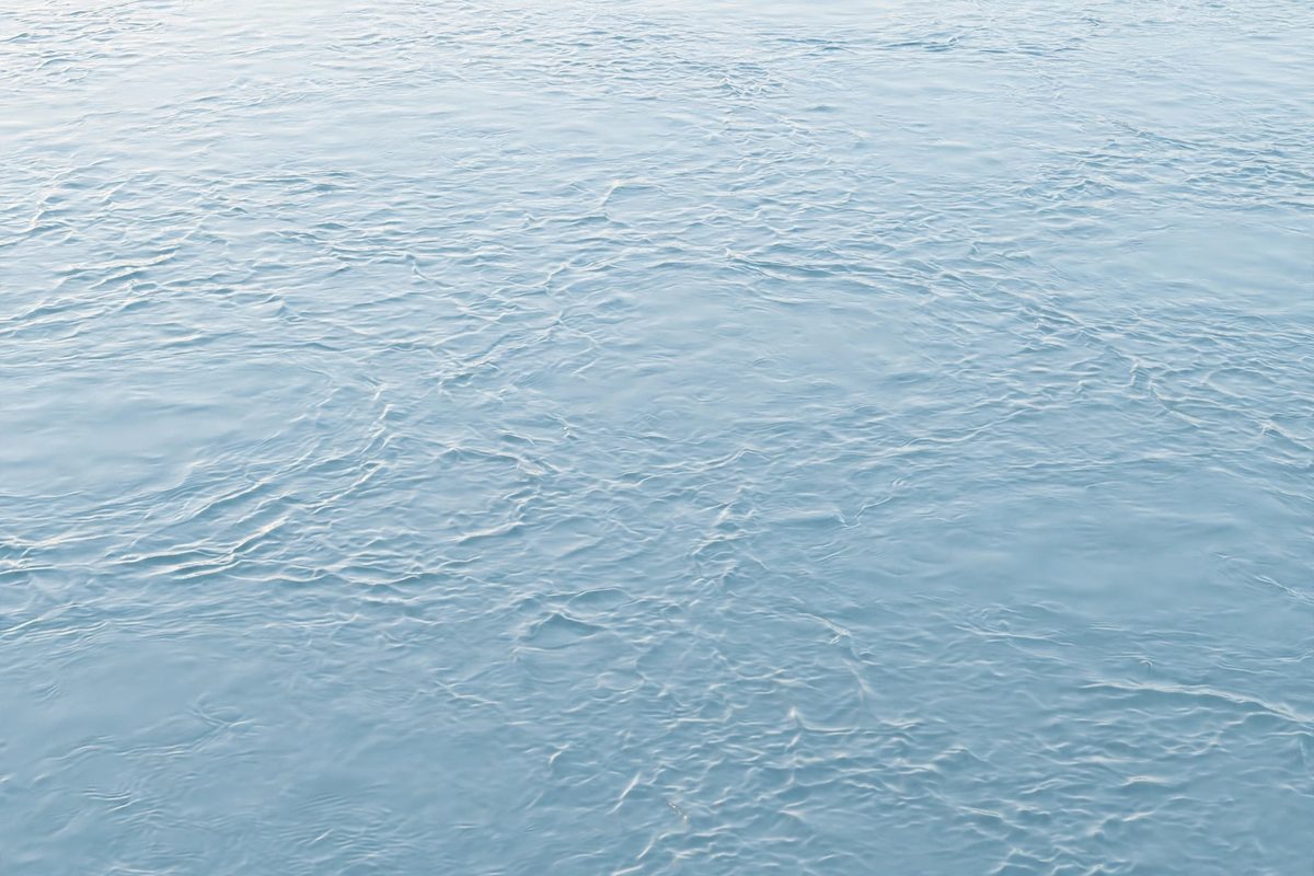 Calm pale blue water surface with gentle ripples in soft light